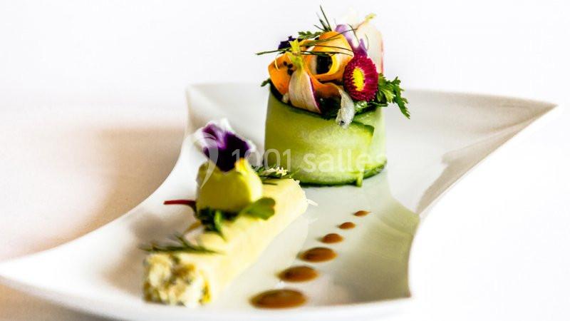 Assiette gastronomique avec roulé de concombre garni de fleurs comestibles et accompagnée d'une présentation soignée.