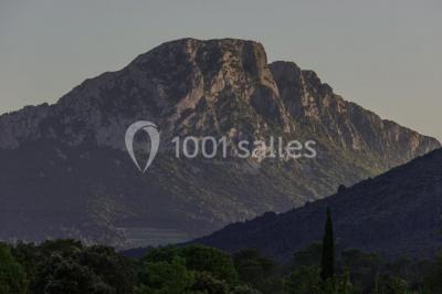 Miniature Location salle Ferrières-les-Verreries (Hérault) - Le Mas de Baumes #18 Montagne rocheuse éclairée par une lumière douce, entourée de collines boisées et d'arbres au premier plan.