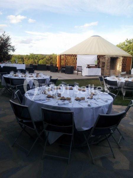 Tables rondes dressées avec nappes blanches et chaises pliantes, en extérieur près d'une tente circulaire.