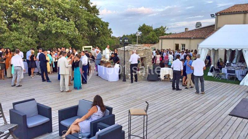 Groupe de personnes rassemblées sur une terrasse en bois, près d'un buffet et d'une tente blanche, lors d'un événement en…