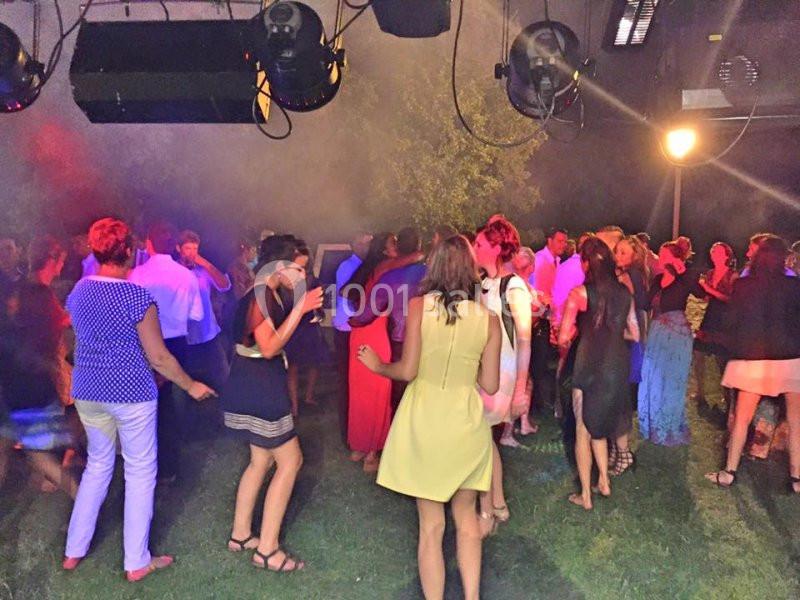 Personnes dansant et discutant lors d'une soirée en extérieur, éclairée par des lumières colorées.