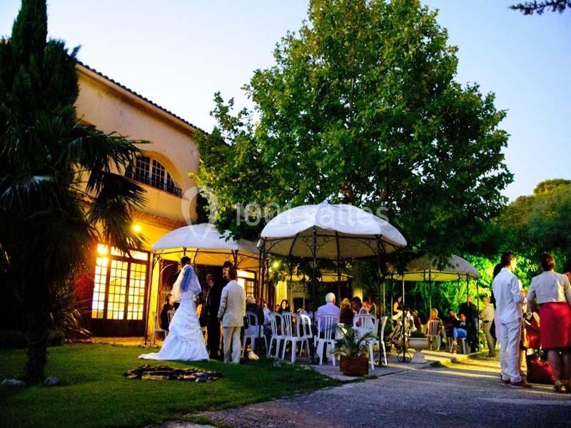 Mariage en extérieur au crépuscule, avec invités assis sous des tonnelles près d'un bâtiment éclairé.