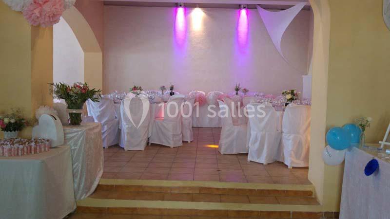 Salle décorée pour un événement avec des tables dressées, des chaises blanches et des éclairages violets.