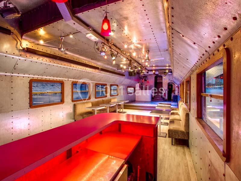 Intérieur d'un wagon aménagé en espace convivial avec bar rouge, tables, banquettes et éclairage chaleureux.