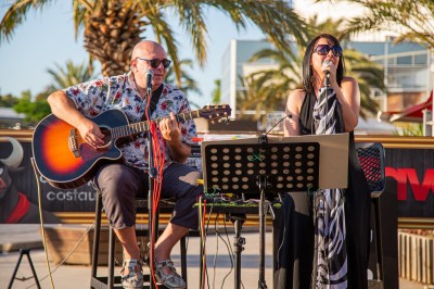 Miniature DJ Pézilla-la-Rivière (Pyrénées-Orientales) - Cleanjack #4 Un duo musical se produit sur une scène intérieure avec guitare et chant, devant un public assis.