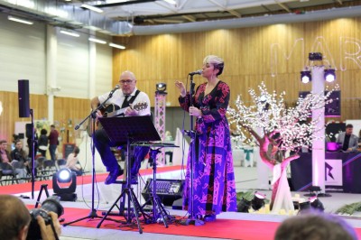 Miniature DJ Pézilla-la-Rivière (Pyrénées-Orientales) - Cleanjack #10 Un duo musical se produit sur une scène intérieure avec guitare et chant, devant un public assis.