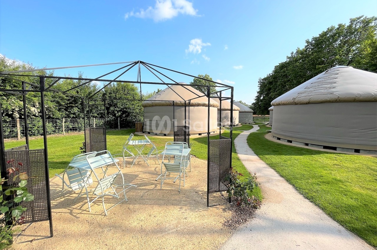 Espace extérieur avec pergola, chaises et tables, entouré de yourtes sur une pelouse bien entretenue.