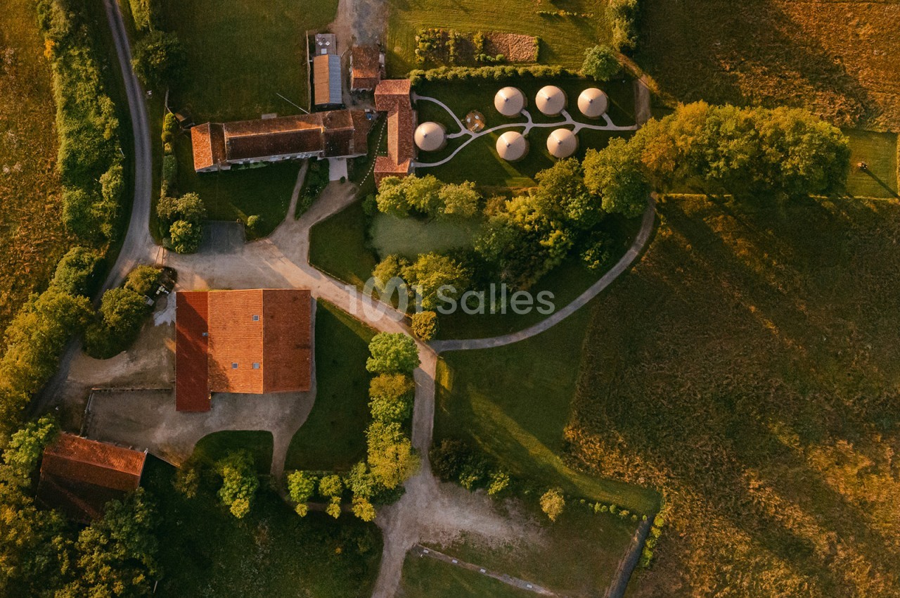 Vue aérienne d'un domaine rural avec bâtiments en tuiles rouges, espaces verts et structures circulaires.