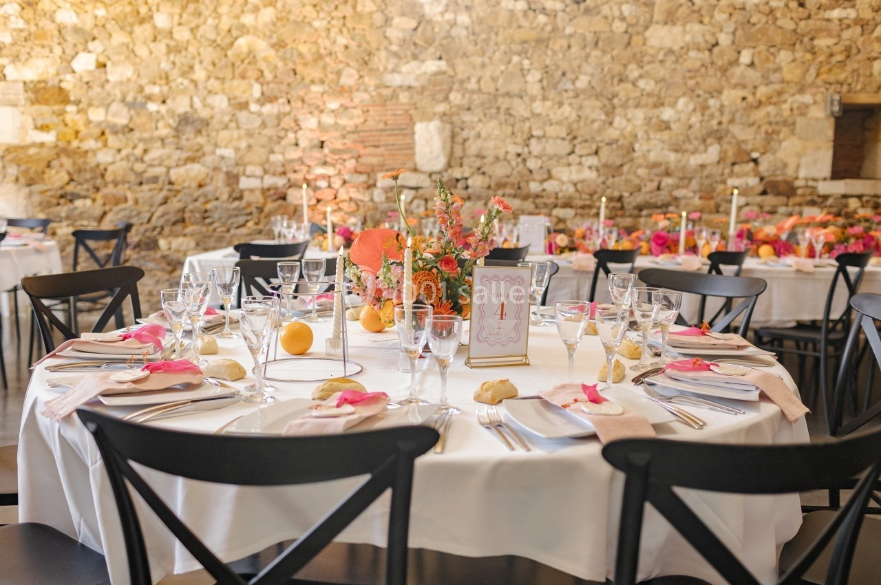 Table ronde décorée pour un événement, avec nappes blanches, fleurs colorées, bougies et vaisselle élégante.