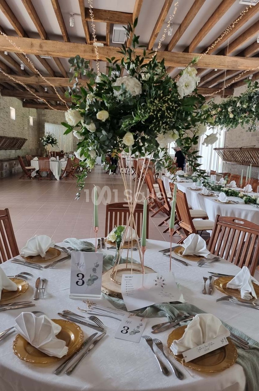 Salle de réception décorée avec des tables élégantes, nappes blanches, centres de table fleuris et chaises en bois.