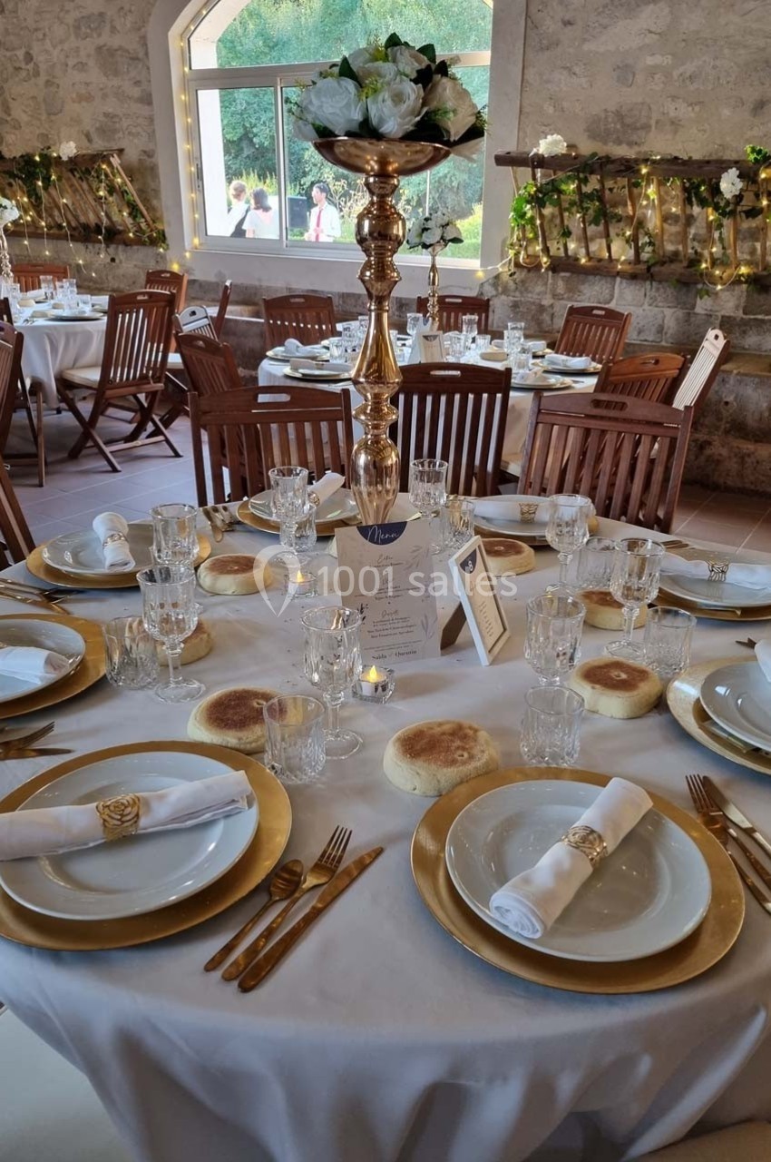 Table de réception élégamment dressée avec vaisselle dorée, serviettes roulées et centre de table fleuri dans une salle en…