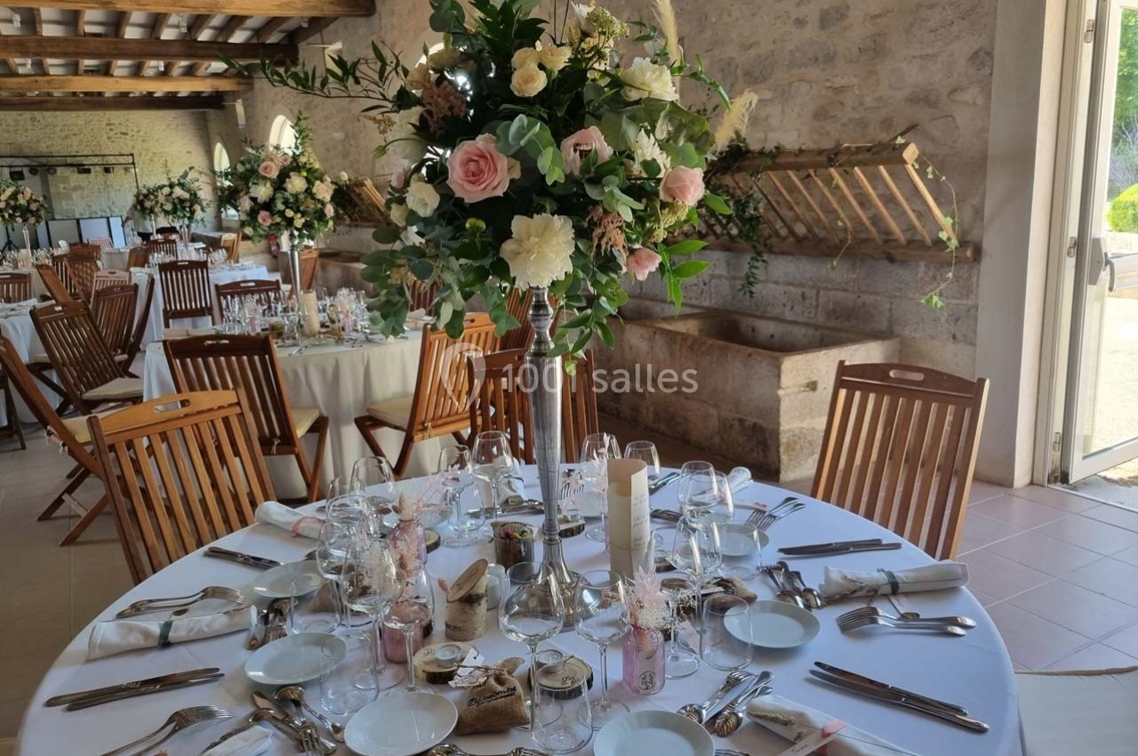 Salle de réception décorée pour un mariage, avec tables rondes dressées et centre de table floral élégant.