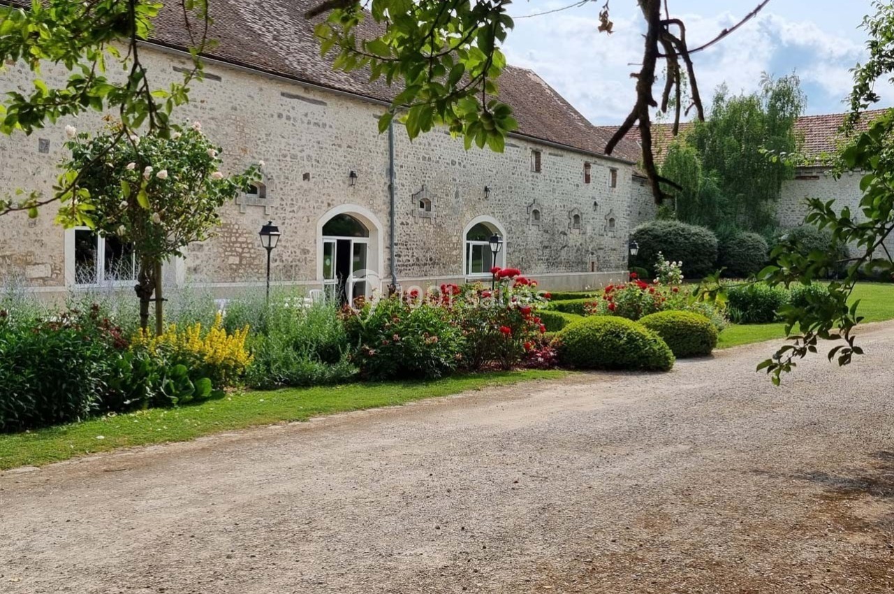 Façade en pierre d'un bâtiment ancien entouré d'un jardin fleuri avec allée gravillonnée au premier plan.