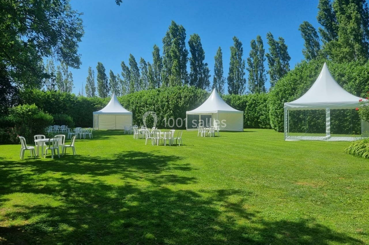 Pelouse verdoyante avec des tentes blanches et des chaises disposées pour un événement en plein air.