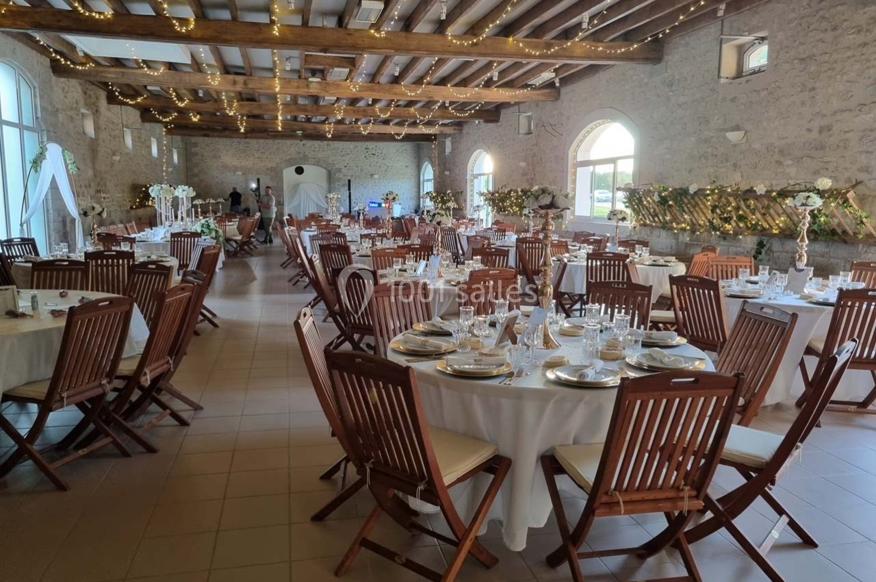 Salle de réception décorée avec des tables rondes dressées, chaises en bois et guirlandes lumineuses suspendues.