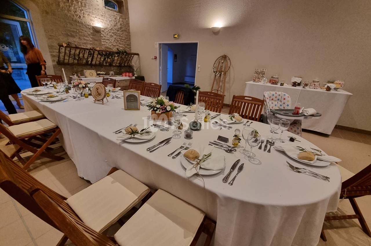 Table dressée pour un repas dans une salle avec murs en pierre, décorations florales et vaisselle disposée.