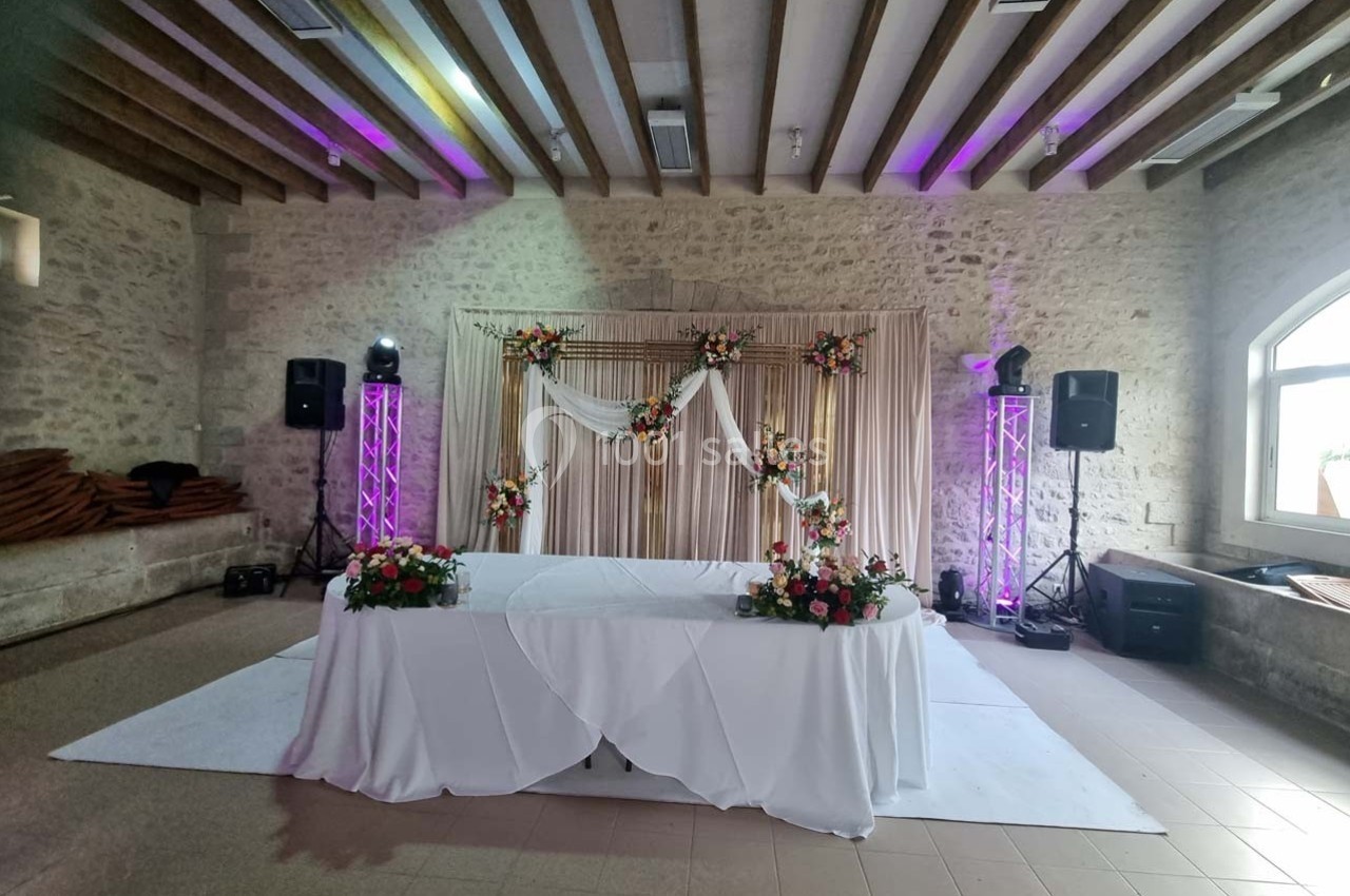 Table décorée avec des fleurs devant une arche ornée de drapés et de compositions florales dans une salle en pierre.