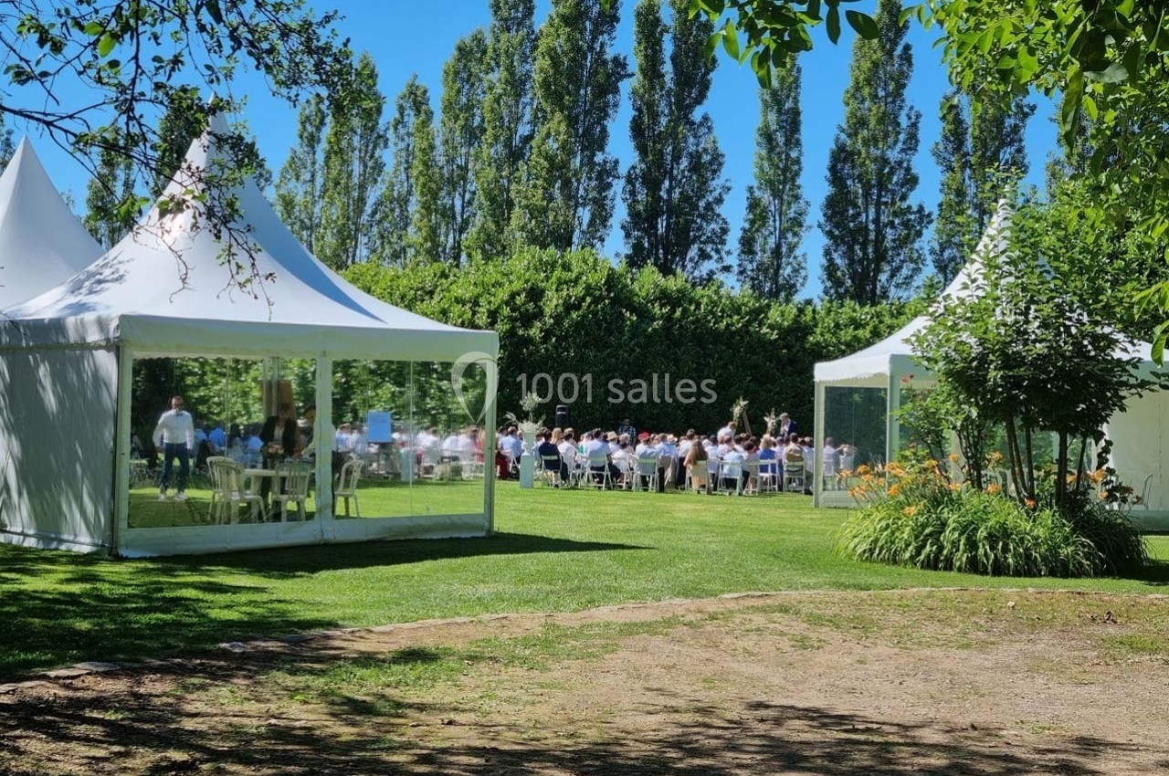 Des invités assis à l'extérieur sous des tentes blanches dans un jardin verdoyant par une journée ensoleillée.