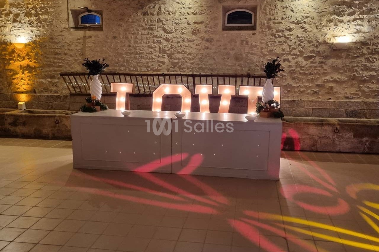 Grandes lettres lumineuses formant le mot ’LOVE’ posées sur un comptoir blanc dans une salle en pierre éclairée.