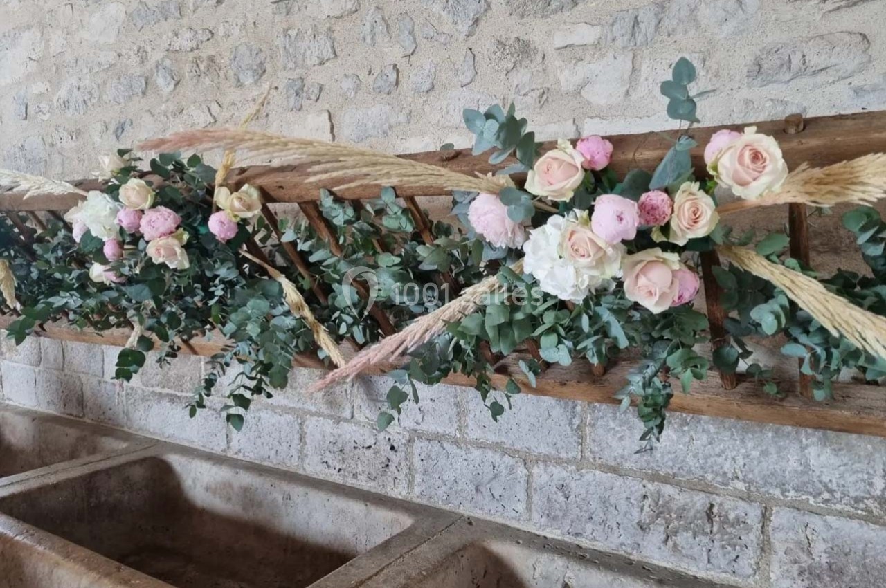 Arrangement floral avec roses blanches et roses, feuillage vert et pampas, décorant une mangeoire en bois dans un cadre…