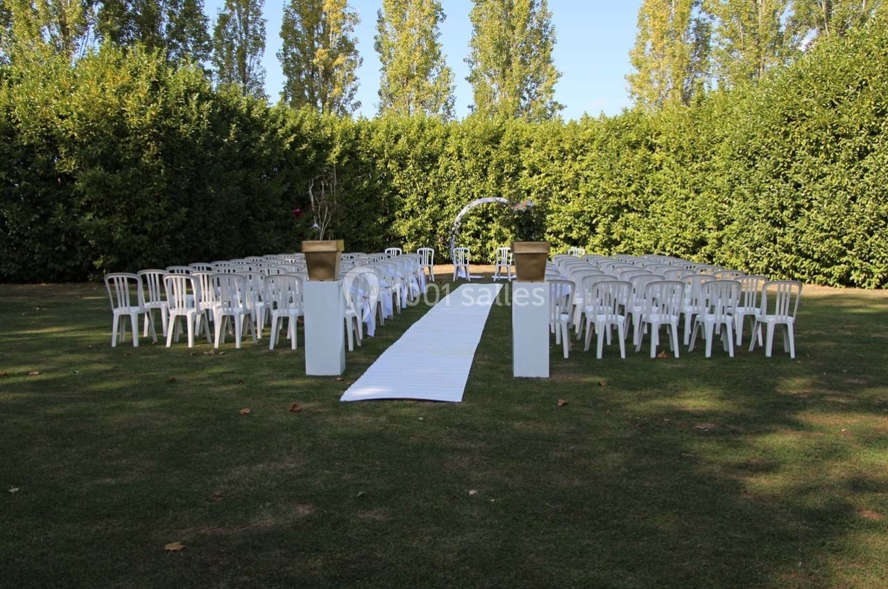 Chaises blanches disposées en rangées de part et d'autre d'une allée centrale sur une pelouse, entourées de haies.