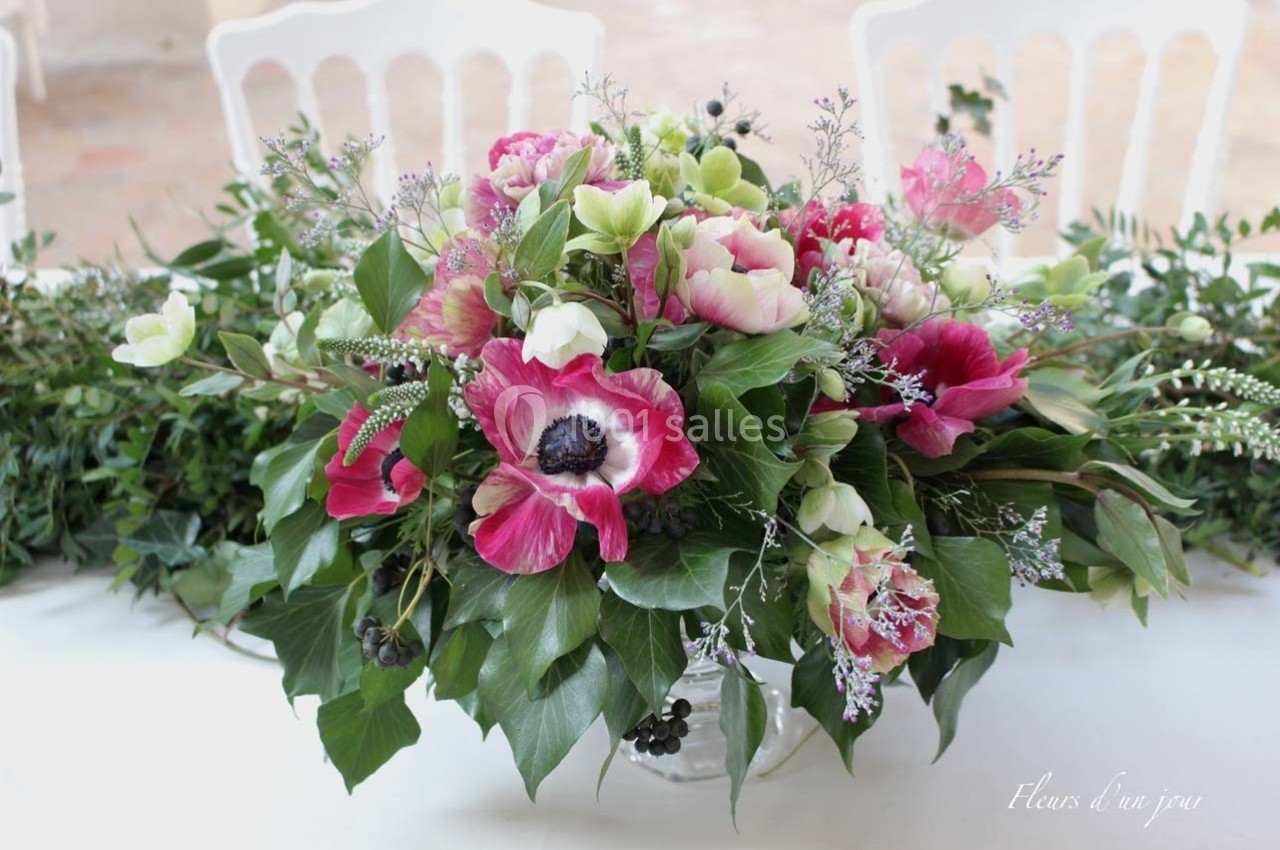 Bouquet de fleurs composé d'anémones roses, feuillage vert et petites fleurs blanches, disposé sur une table blanche.