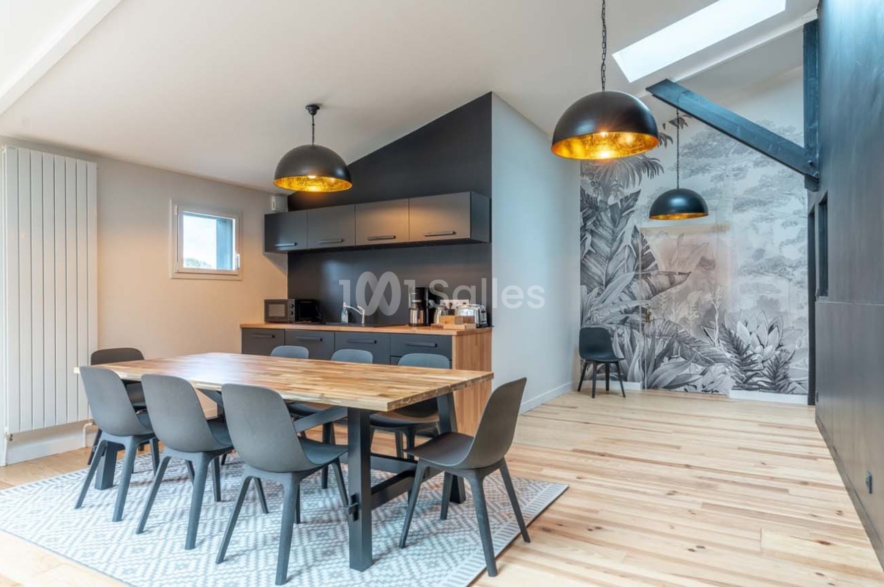 Salle à manger moderne avec table en bois, chaises noires, cuisine ouverte et mur décoré d'une fresque végétale.