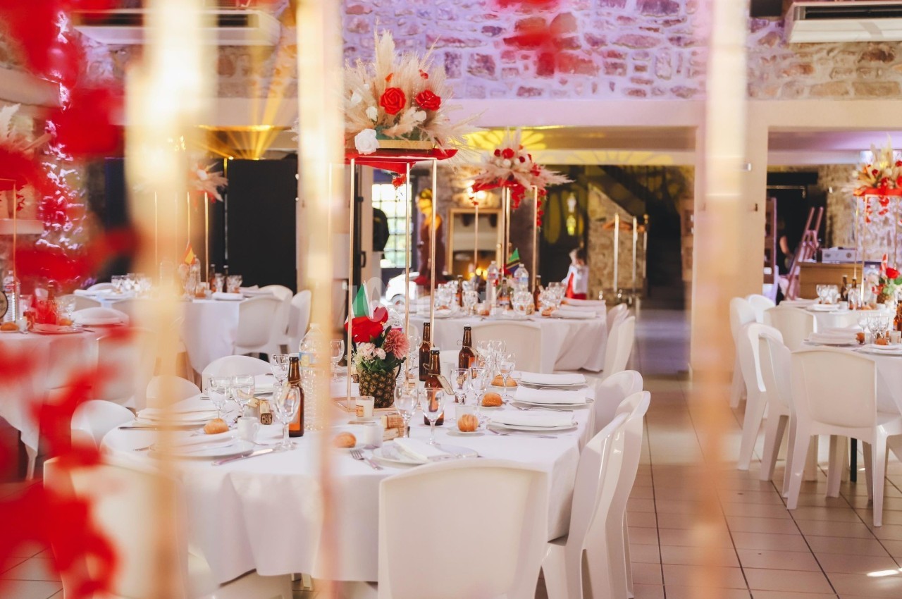 Salle de réception décorée avec des tables rondes, nappes blanches, centres de table floraux et éclairage chaleureux.