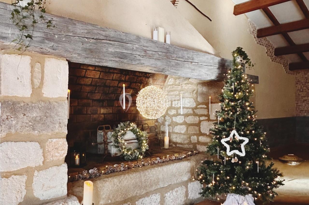 Cheminée en pierre décorée pour Noël avec un sapin illuminé, des bougies et une guirlande lumineuse.