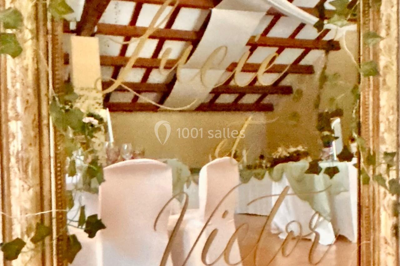 Miroir doré décoré de feuillage, reflétant une salle de réception avec des chaises blanches et un plafond en poutres…