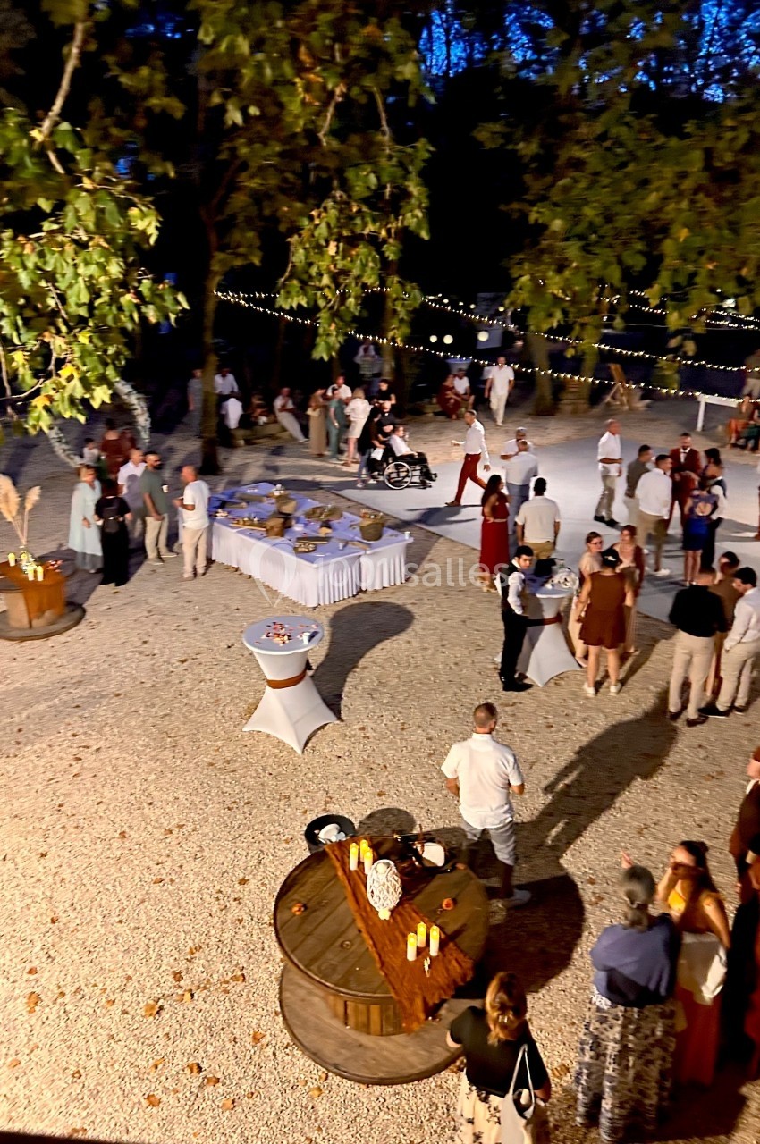 Groupe de personnes réunies en soirée en plein air, avec tables décorées et guirlandes lumineuses suspendues.