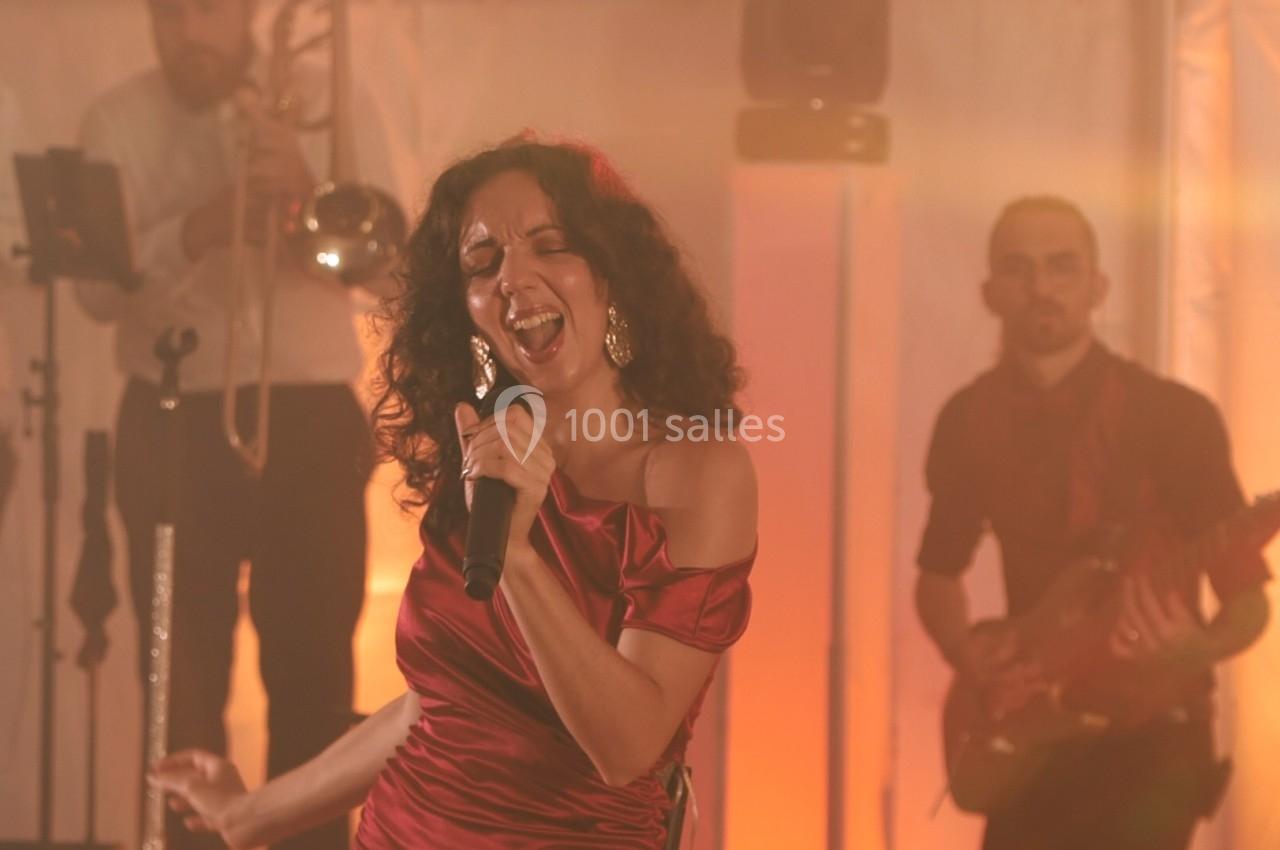 Une chanteuse en robe rouge interprète une chanson sur scène, accompagnée de musiciens en arrière-plan.