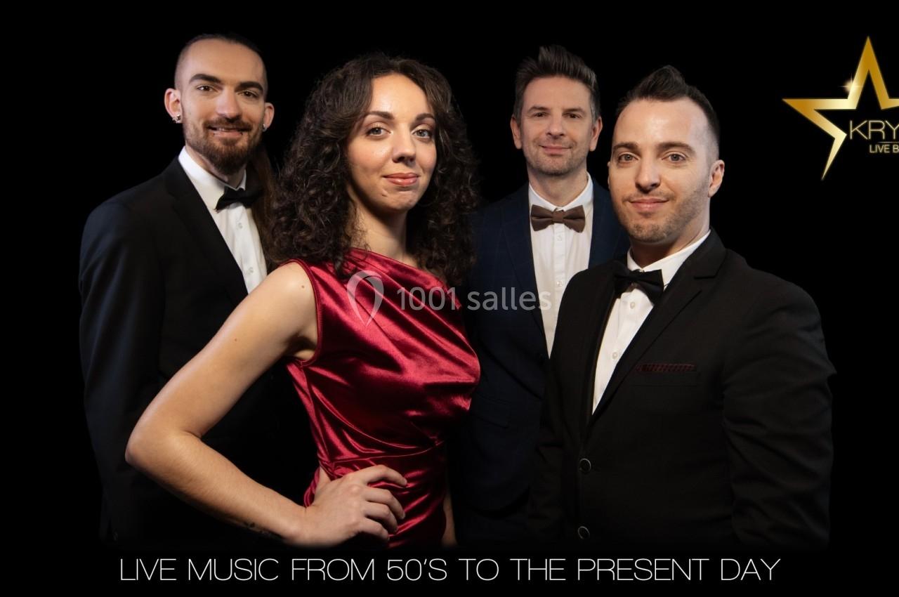 Quatre musiciens en tenue élégante posent devant un fond sombre avec un logo en forme d'étoile dorée.