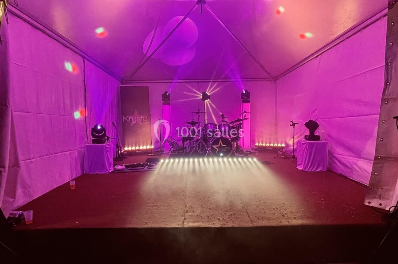 Scène sous chapiteau avec éclairage rose, batterie au centre et projecteurs disposés autour.