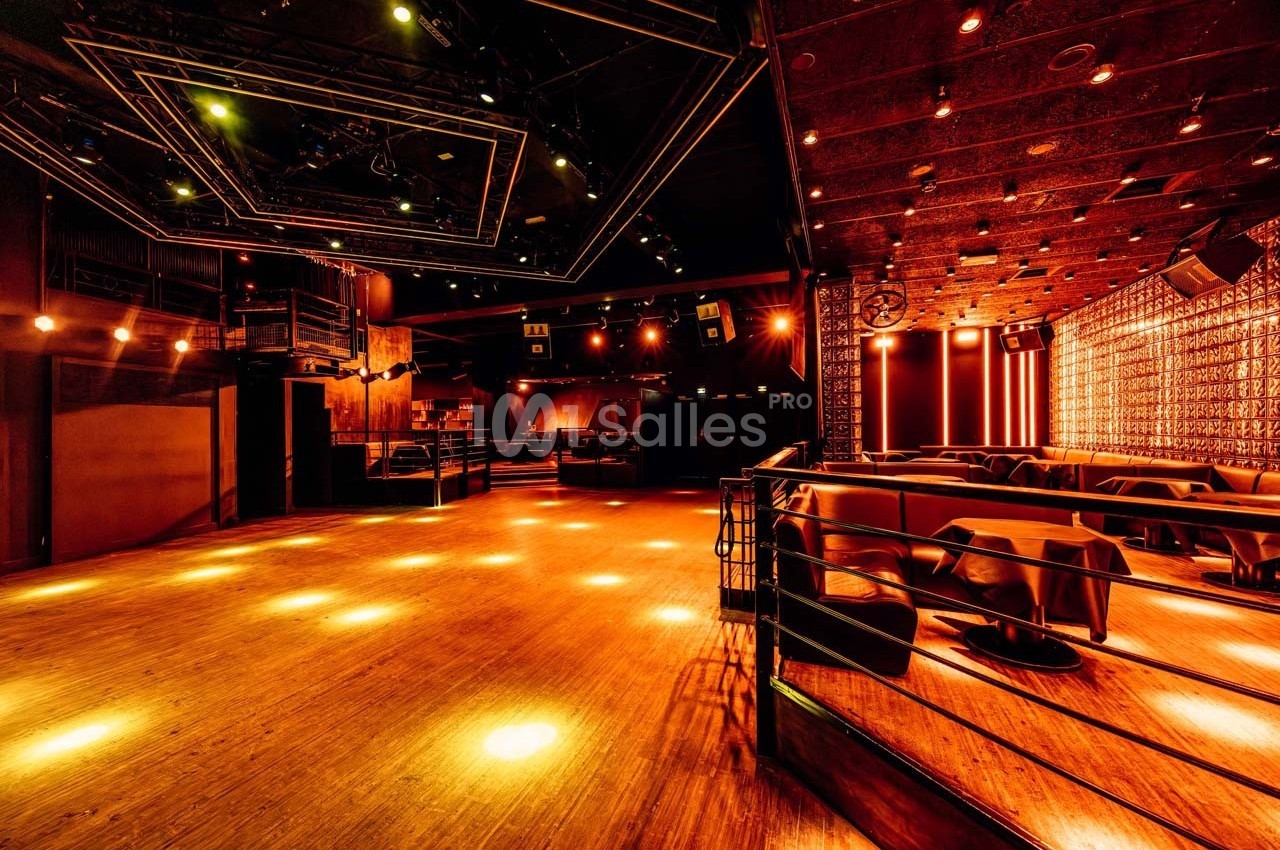 Salle de danse vide avec éclairage tamisé, parquet en bois et tables couvertes le long des murs.