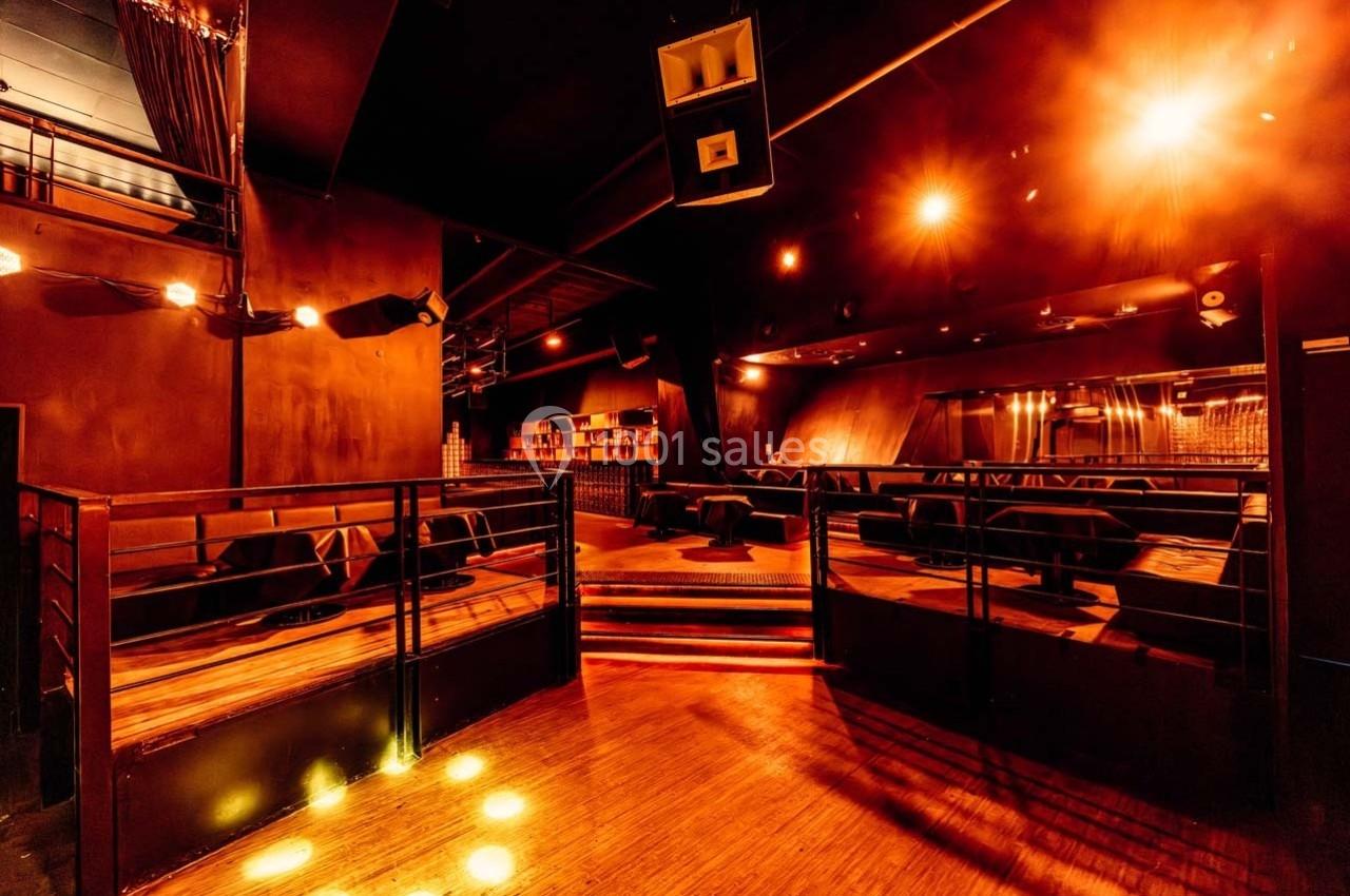 Salle sombre avec éclairage tamisé orange, banquettes alignées, piste en bois et enceintes suspendues.