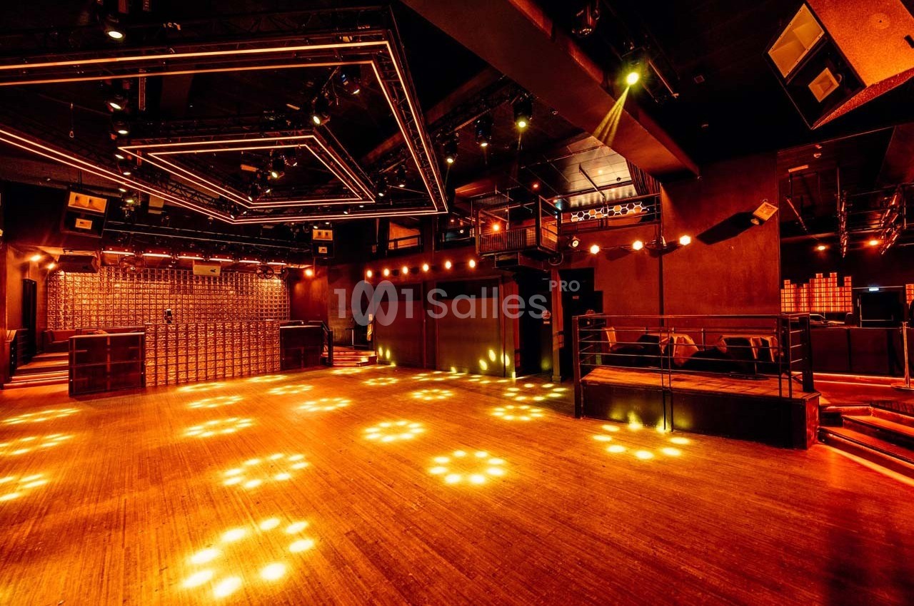 Salle de concert vide avec éclairage chaleureux, parquet en bois et structures lumineuses au plafond.