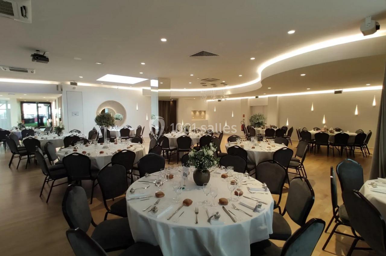Salle de réception élégante avec tables rondes dressées, nappes blanches et décoration florale.