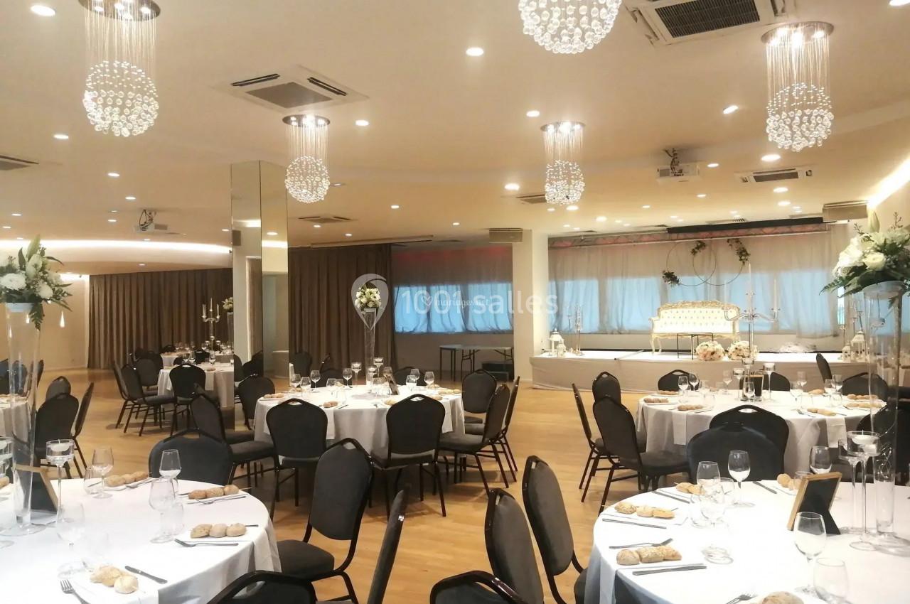 Salle de réception élégante avec tables dressées, chaises noires, décorations florales et lustres suspendus.