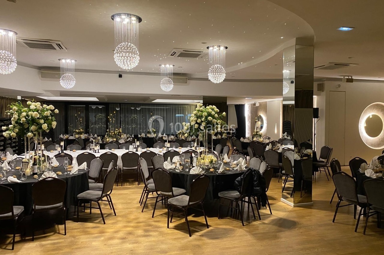 Salle de réception élégamment décorée avec tables rondes, nappes noires, chaises noires et centres de table fleuris.