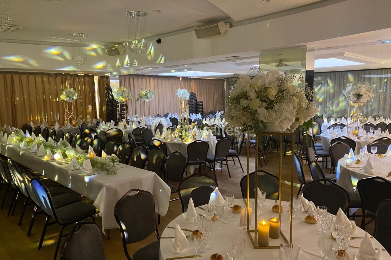Salle de réception décorée pour un événement, avec tables dressées, nappes blanches, chandelles et compositions florales.