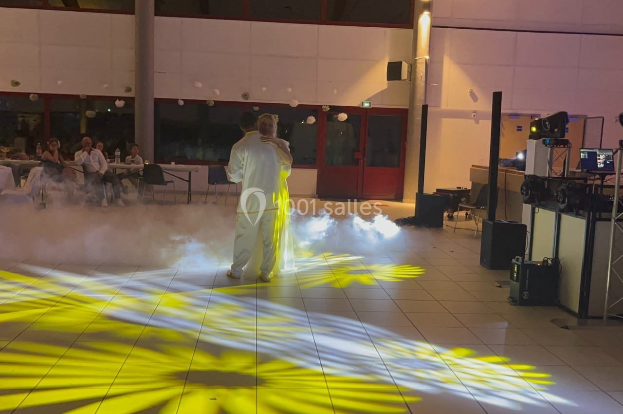 Un couple danse au centre d'une salle éclairée par des projecteurs jaunes, avec de la fumée au sol.