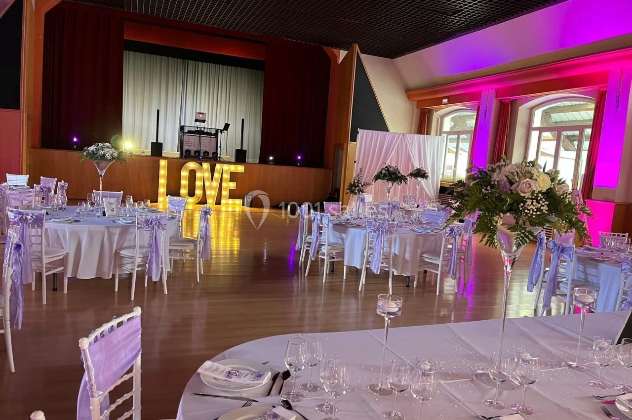 Salle de réception décorée pour un mariage, avec tables dressées, fleurs, éclairage coloré et lettres lumineuses ’LOVE’.
