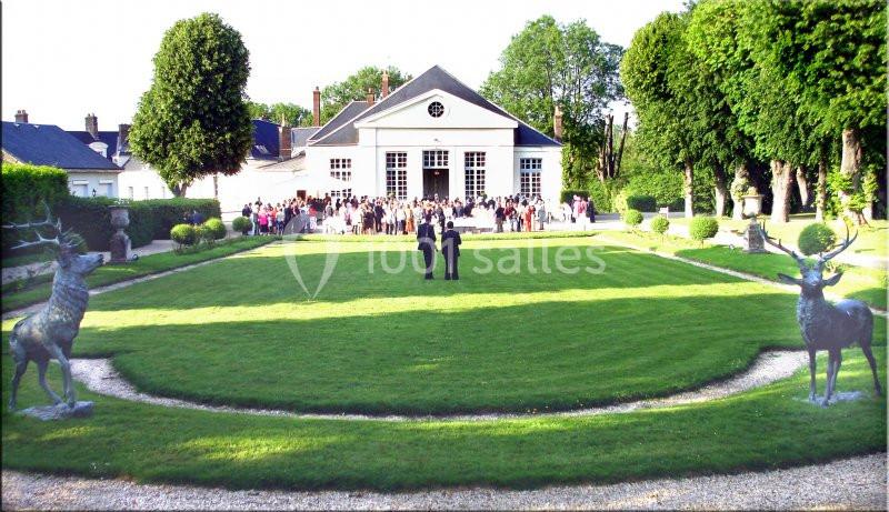 Jardin avec pelouse centrale, statues de cerfs et bâtiment en arrière-plan, groupe de personnes rassemblées devant.