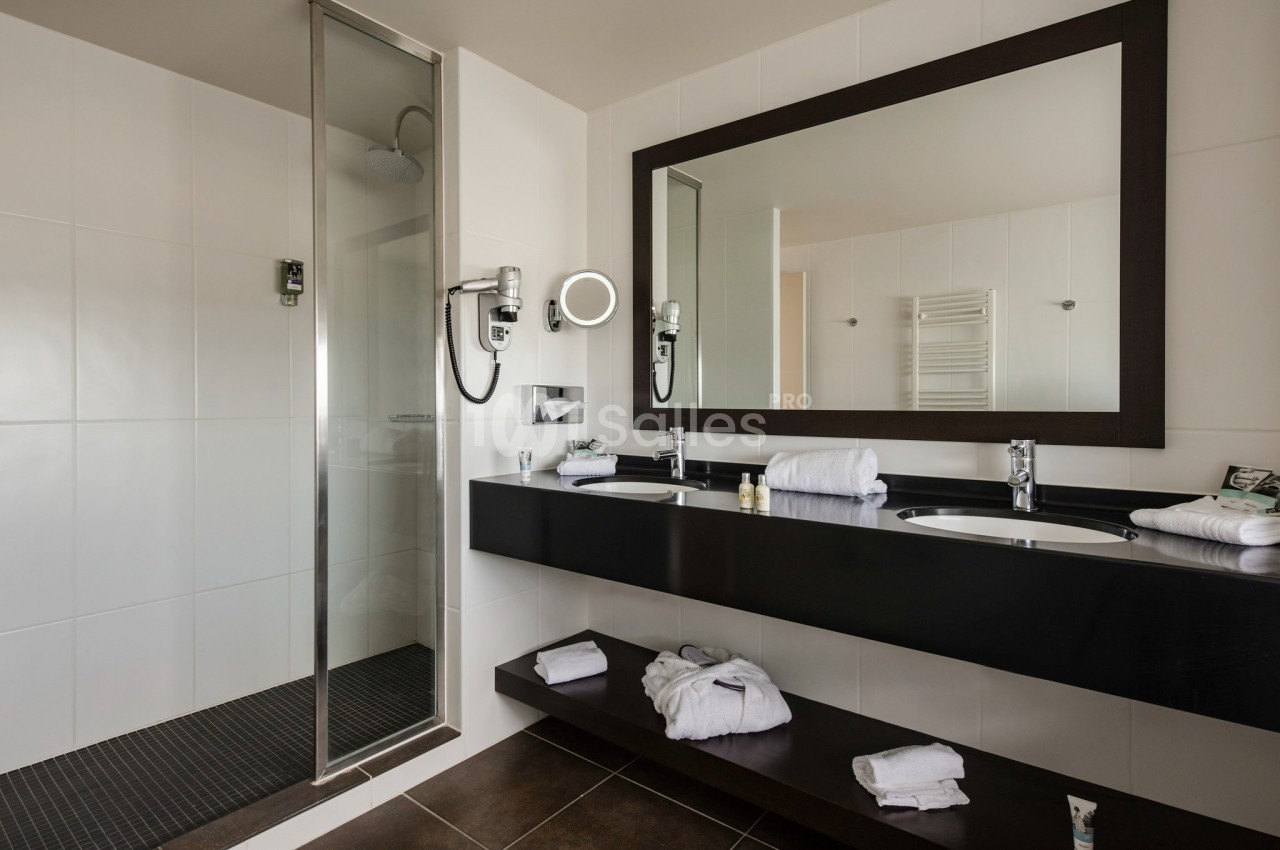 Salle de bain moderne avec douche à l'italienne, double vasque, miroir encadré et serviettes disposées sur les étagères.