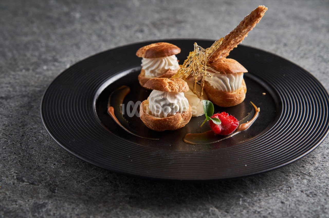 Assiette de profiteroles garnies de crème, décorées de caramel filé, d'une framboise et d'une feuille verte.