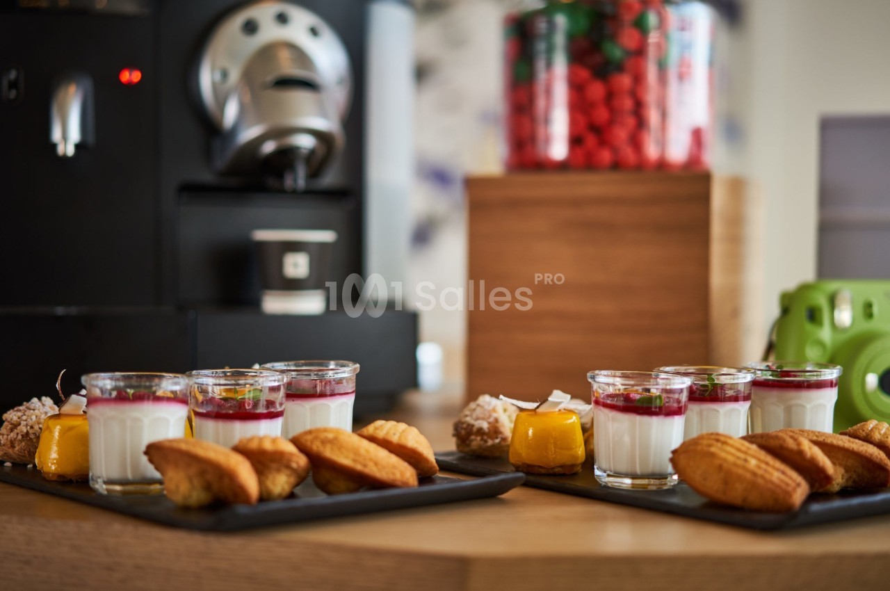 Plateaux de desserts comprenant verrines, madeleines et autres douceurs, disposés près d'une machine à café.