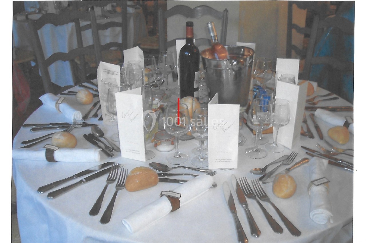 Table dressée pour un repas avec nappes blanches, couverts, verres, menus, pains, bouteille de vin et seau à glace.