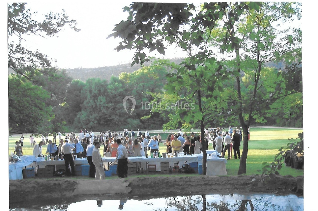 Groupe de personnes réunies dans un parc verdoyant, avec des tables dressées et un plan d'eau au premier plan.