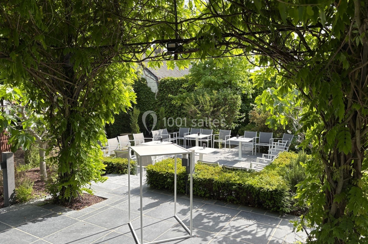 Terrasse extérieure ombragée avec des tables et des chaises entourées de végétation verdoyante.